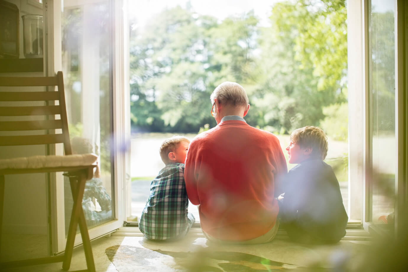 Gro&szlig;vater und Enkel sitzen im T&uuml;rrahmen mit Blick in den Garten