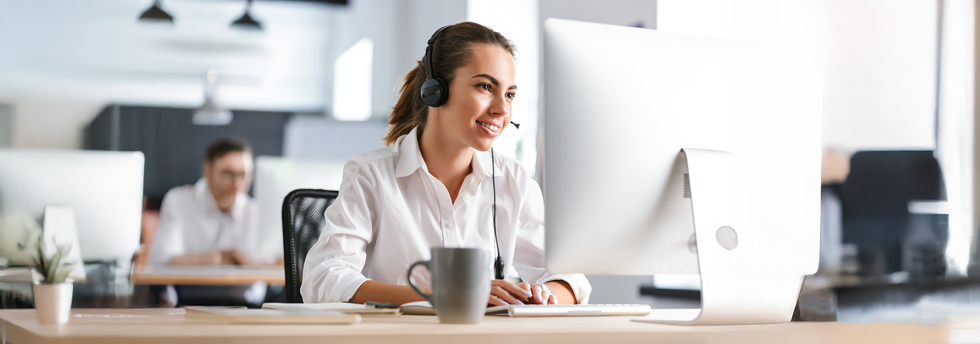 Person mit Kopfh&ouml;rern arbeitet am Computer, Tasse auf dem Tisch.