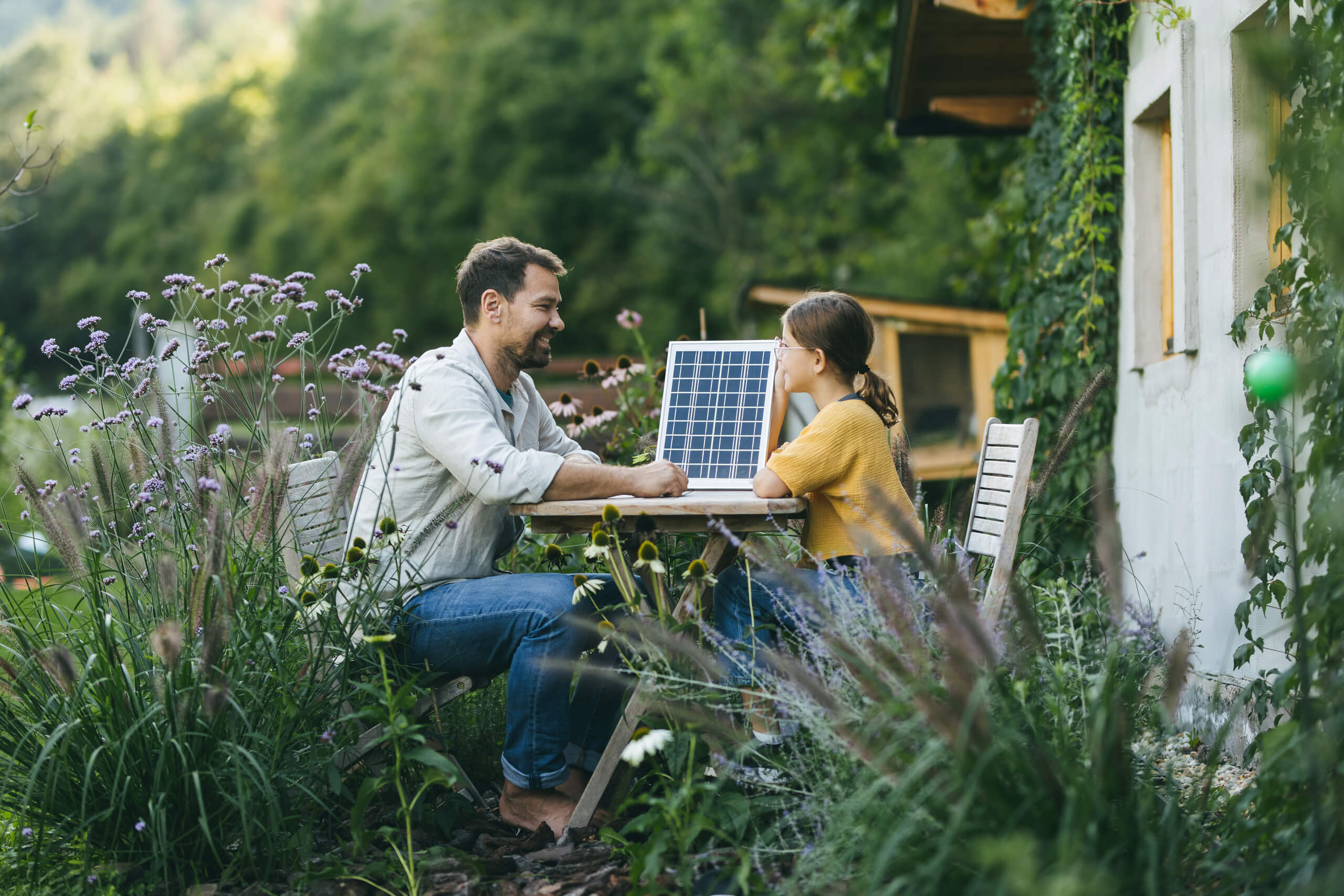 Vater mit Tochter im Garten sitzend, mit Modell eines Solarpanels