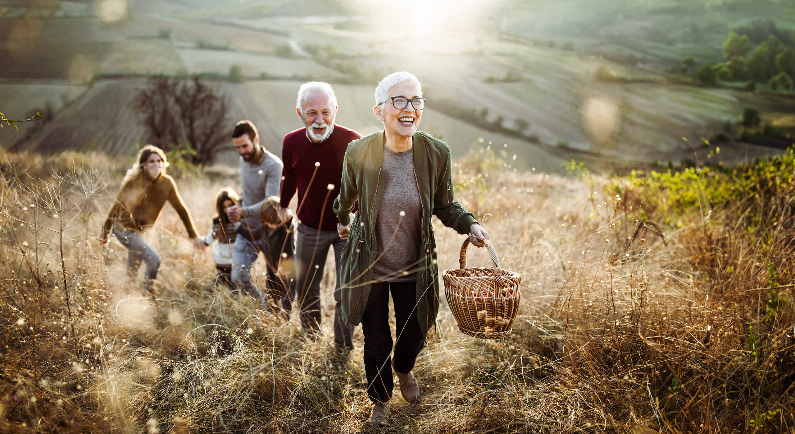 Gl&uuml;ckliche Seniorin f&uuml;hrt Familie zum Picknick im Feld