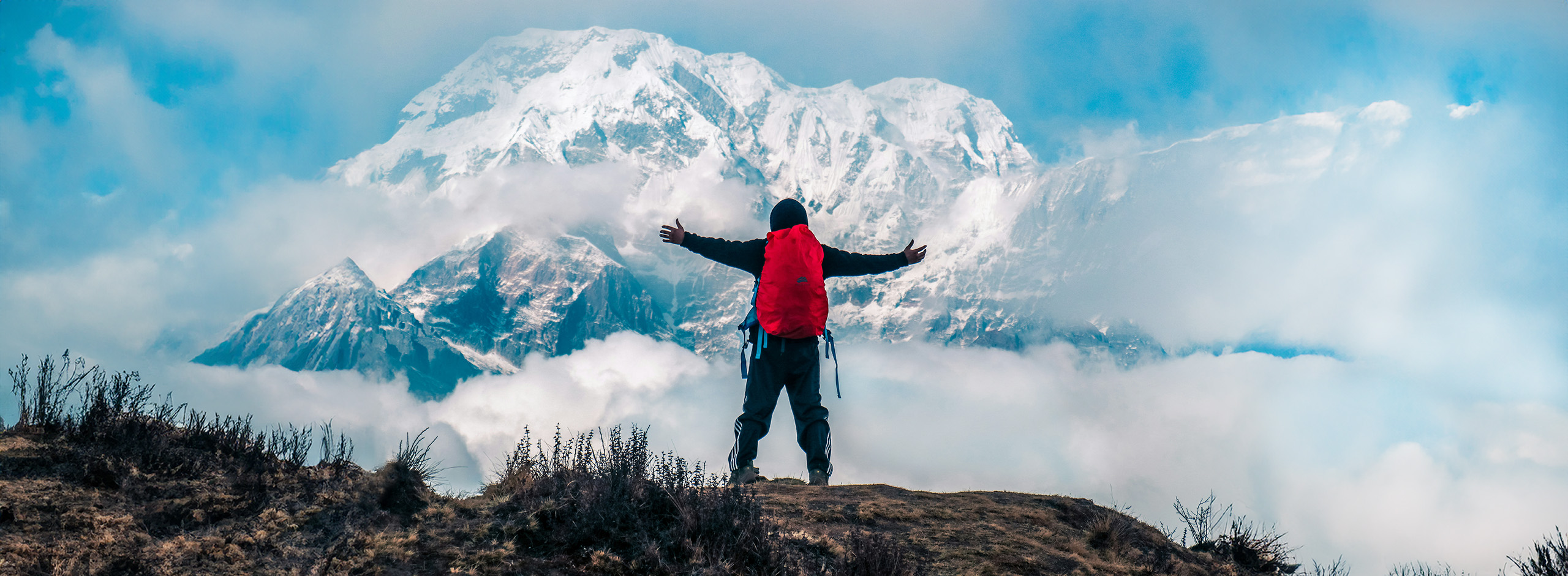 Wanderer mit rotem Rucksack breitet seine Arme aus vor Bergkulisse