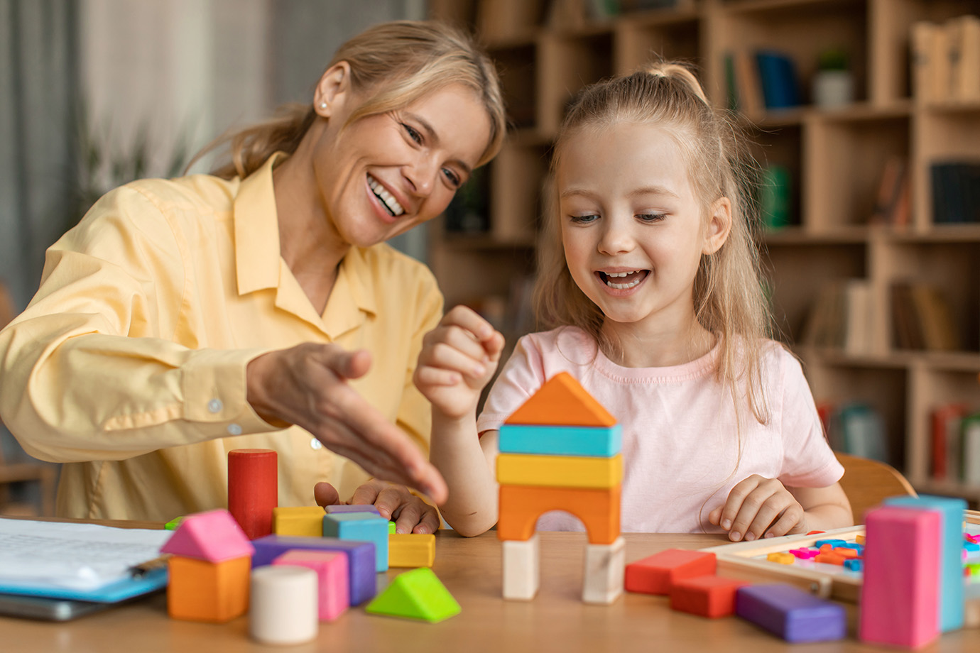 Erzieherin spielt mit M&auml;dchen mit Holzbausteinen