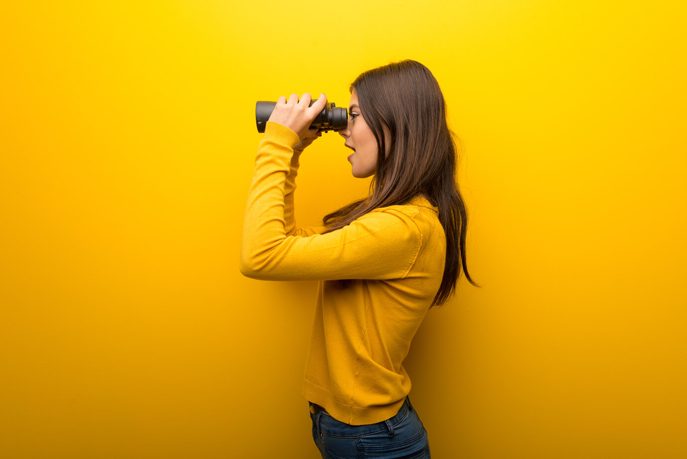 Frau auf leuchtend gelbem Hintergrund und Blick in die Ferne mit einem Fernglas