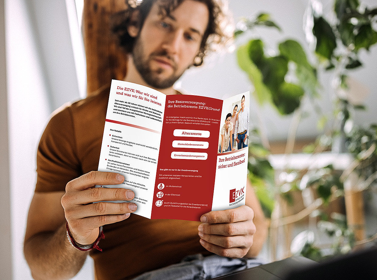 Ein Mann sitz an seinem Schreibtisch und liest in einem EZVK-Flyer