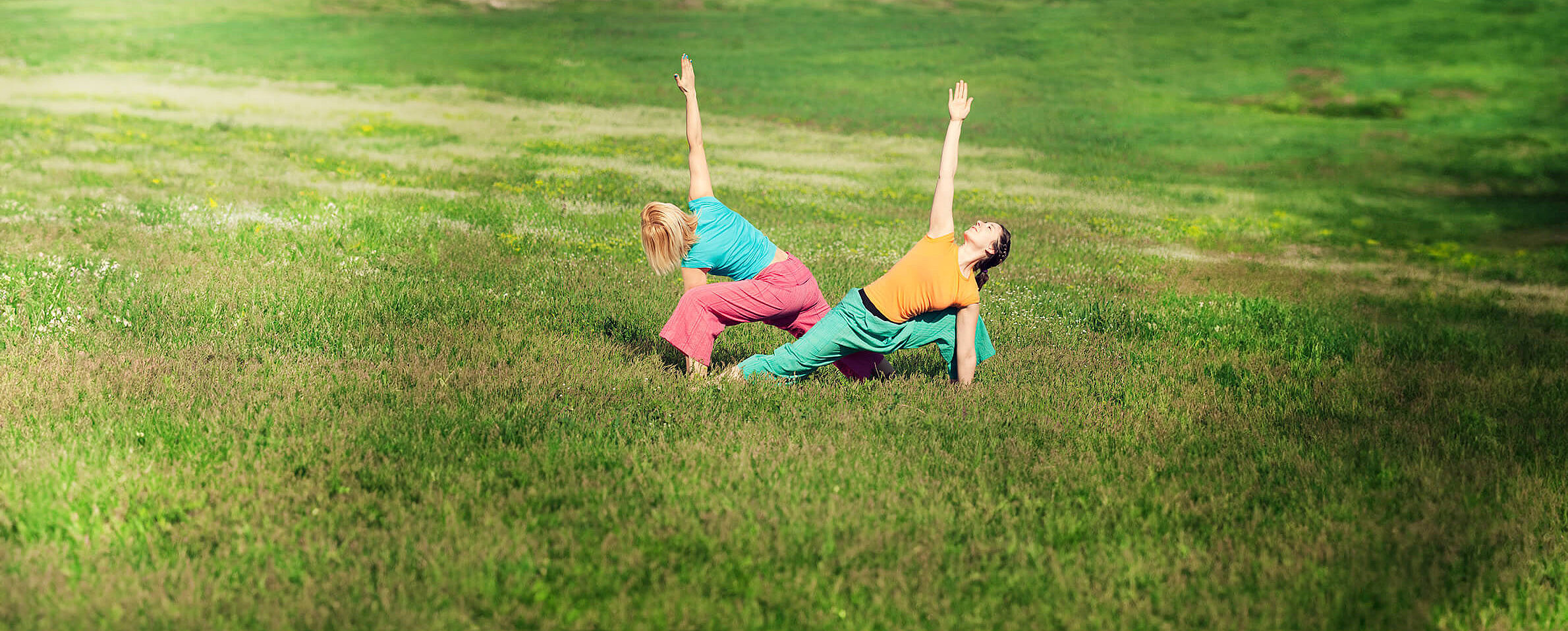 Zwei Frauen machen Yoga&uuml;bungen auf einer Wiese