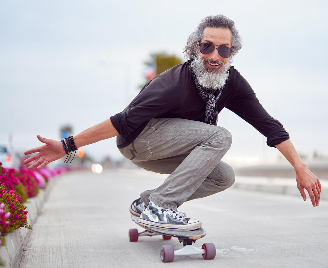 Reifer Mann mit wei&szlig;em Bart f&auml;hrt Skateboard