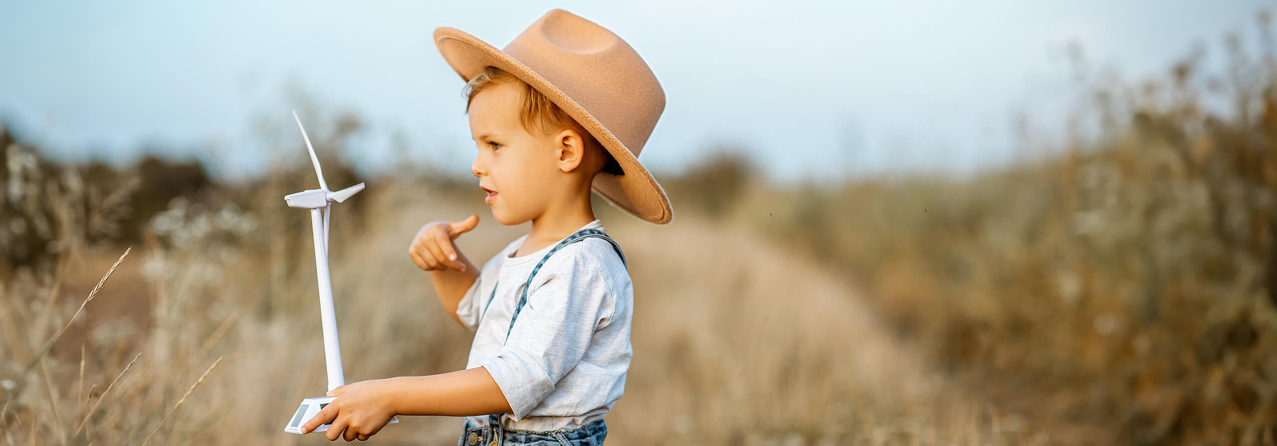 Junge steht auf einem Feld mit kleinem Windrad in der Hand